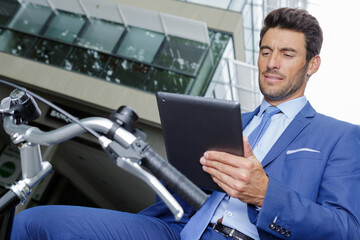 young businessman checking his tablet while on a bicycle