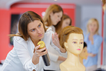 trainee hairdresser spraying mannequins hair with hairspray