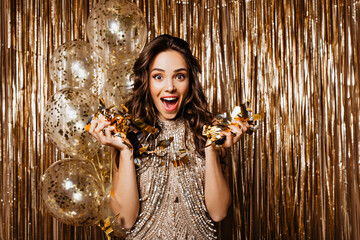Obraz premium Girl with dark hair throws confetti and rejoices on golden background