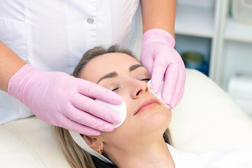 cosmetology. Close up picture of lovely young woman with closed eyes receiving facial cleansing procedure in beauty salon.