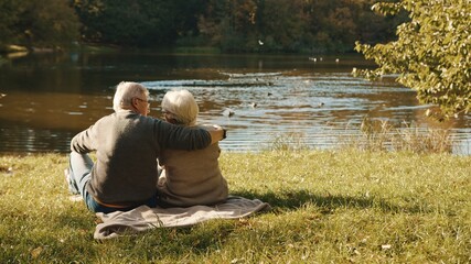 Elderly gray haired couple siting on the bench near the river on autumn day. High quality photo