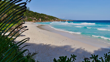 Panoramic view of tropical beach Petite Anse with turquoise colored water, granite rock formations and strong waves.