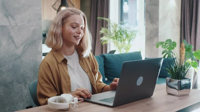 Modern blonde young woman working from home social distancing. Attractive girl speaking online videochatting job application interview with employer via laptop computer.