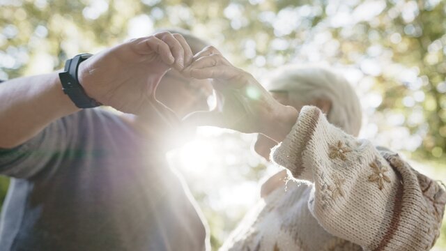 Lovely older retired couple making heart with their hands and looking at each other. Selective focus. High quality photo