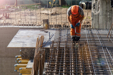 workers using steel wire and pincers to secure rebar before concrete is poured over it.
