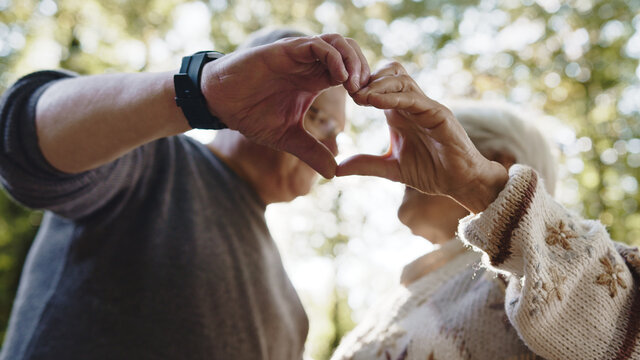 Lovely older retired couple making heart with their hands and looking at each other. Selective focus. High quality photo
