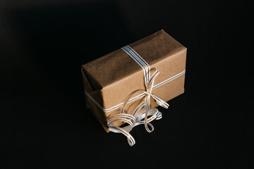 Gift box wrapped in recycled craft paper and tied with a white and gold ribbon bow on a black background. Surprise for the holiday