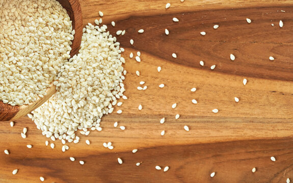 White Sesame Seeds Pouring From Small Cup To Wooden Table, View From Above