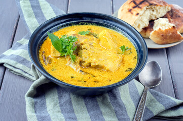 Traditional Indian fish curry with pita bread offered as close-up in a design in bowl