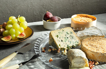 Various types of French cheeses - camembert, roquefort, brie, goat cheese and epoisse with grapes, figs and nuts on a gray background