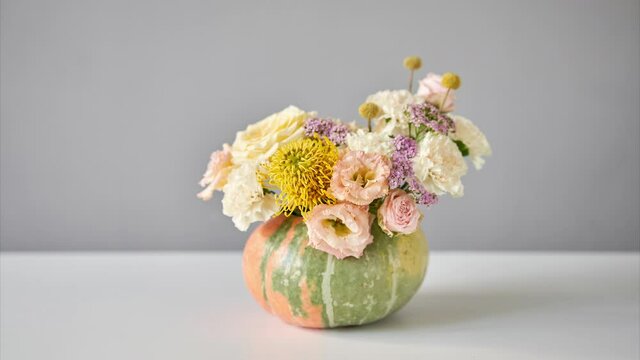 Stop motion, step by step installation of flowers arrangement in pumpkin on the white table. Fresh cut flowers for decoration home. European floral shop. Delivery fresh cut flower.