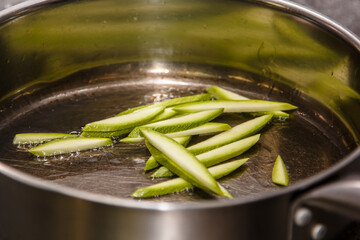 The chef is frying zucchini sliced into thin slices in oil in a frying pan