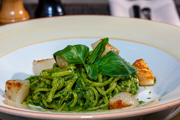 Pasta (spaghetti) with pesto sauce and scallops is on the plate.