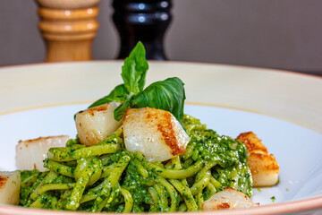 Pasta (spaghetti) with pesto sauce and scallops is on the plate.
