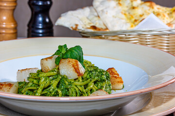 Pasta (spaghetti) with pesto sauce and scallops is on the plate.