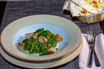 Pasta (spaghetti) with pesto sauce and scallops is on the plate.
