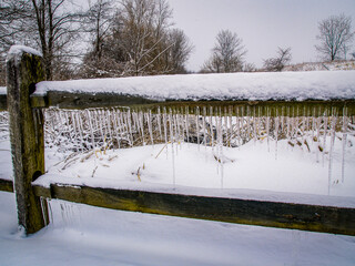 Snow covered wooden split-rail fence draped with icicles.