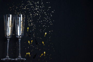 Two champagne glasses, golden confetti on a festive black background. Festive Christmas, New Year concept. Copy space.