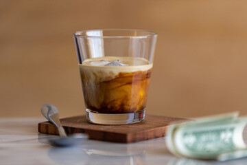 Coffee break. Ice espresso with cream in a glass, spoon, money, copy space.