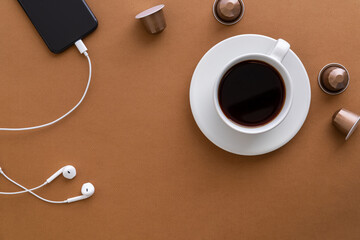 Flat lay with coffee cup, coffee capsules, earphones and a cell phone on brown background. Copy space.