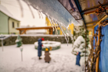 Icicles hanging from house roof in a garden with a blurry family in the background - typical winter...