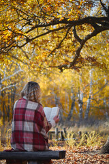 Beautiful european woman in autumn park sitting under a tree and reading a book