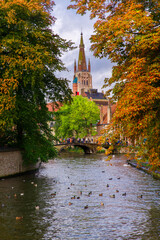 Bruges, Flanders, Belgium, Europe - October 1, 2019. Channels with white swans in the autumn of Bruges (Brugge) with the church of Our Lady in the background