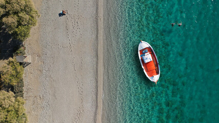 Aerial drone top down photo of traditional red wooden boat in turquoise clear beach of Ganema in island of Serifos, Cyclades, Greece 