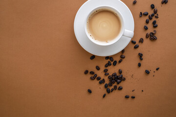 Flat lay with cup filled with coffee with cream and coffee beans on brown background. Copy space.
