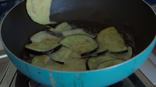 Preparing something to eat for lunchtime at home. Sliced eggplants are fried in a pan with boiling oil.