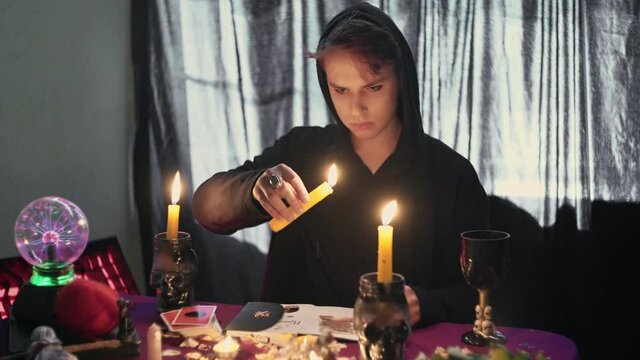 Male fortune teller psychic holding a magic pendulum over a candle and looks at photo with lost person