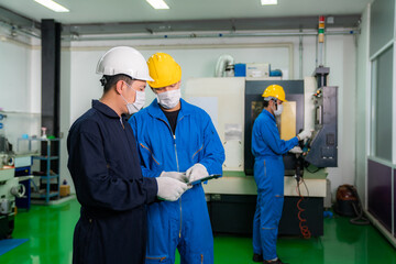 Asian industrial engineers and worker in hard hats discuss product line while using digital tablet and make showing gestures and work in a heavy industry manufacturing factory.