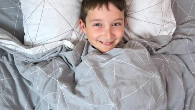A smiling lauthing boy lying in bed in the morning, happy joyful child concept