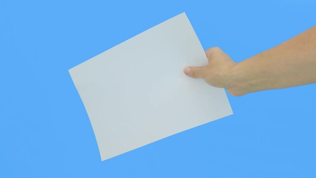 A hand holding a white empty piece of paper A4 with copy space against blue background