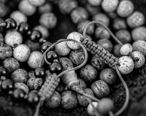 Black and white close of three strings of beads of different shades. Detail of beads and knots in thread