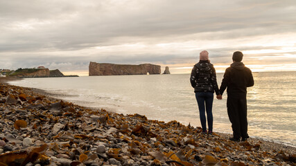 Back view of a couple holding hands and admiring the Percé Rock, in Canada