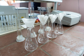 Row of glass measurement flasks with paper filters inside on a ceramic laboratory table