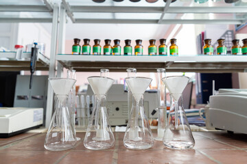 Row of glass measurement flasks with paper filters inside on a ceramic laboratory table