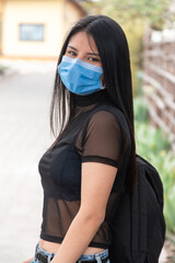 closeup of beautiful young latin woman with long black hair, standing, wearing a mask, transparent blouse, outdoors