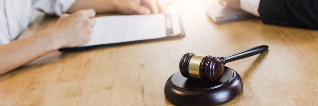 Hamer of justice on table, Legal law, advice concept, Professional male lawyers working on courtroom sitting at the table and explain before signing papers with gavel and scales of justice.