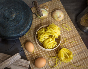Chapa de fogão a lenha com panela de pedra e esteira de bambu com macarrão cru, ovos, lenha e cebola de cabeça.