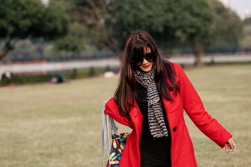 Education, high school and people concept - happy smiling young woman in glasses over green outdoor background. She is carrying her bag and wearing red dress for winter.