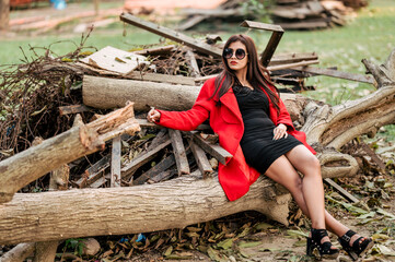 Attractive young woman wearing black sunglasses and red coat. Outdoor shot on wooden background. Beauty and fashion concept.