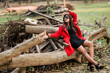 Attractive young woman wearing black sunglasses and red coat. Outdoor shot on wooden background. Beauty and fashion concept.