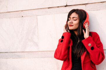 Young woman using smartphone and listening music on headphone. Outdoor image with Asian/ Indian model with extra copy space.