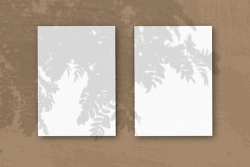 2 vertical sheets of textured white paper on brown table background. Mockup overlay with the plant shadows. Natural light casts shadows from a Rowan branch. Horizontal orientation