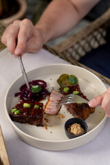 Man is eating beef loin in teriyaki sauce, cutting it with knife and fork, close up on a white tablecloth background