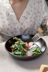 Young pretty woman is eating a gourmet salad with duck and lettuce with knife and fork, mixing it, summer terrace in a posh restaurant