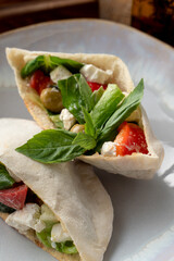Close up of pita with salad, feta cheese and olives decorated with basil leave on a white plate, close up