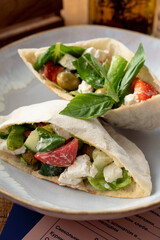Close up of pita with salad, feta cheese and olives decorated with basil leave on a white plate, close up